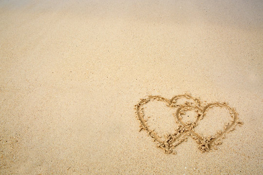Two hearts drawn on the sand of a beach.