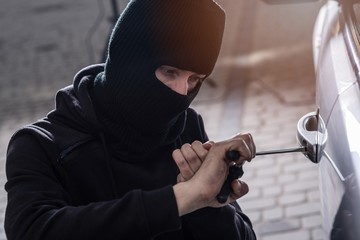 Auto thief in black balaclava trying to break into car
