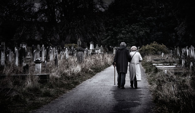 Brompton, London - An elderly couple walk hand-in-hand through a graveyard