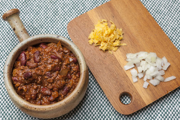 Bowl of chili with cheese and onions on side.