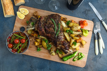 Roast lamb shoulder with roasted potatoes and carrots styled in a rustic wooden board, top view