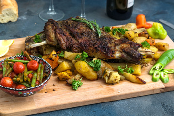 Roast lamb shoulder with roasted potatoes and carrots styled in a rustic wooden board, top view