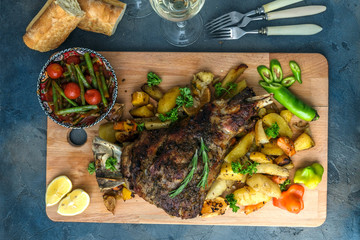 Roast lamb shank with roasted potatoes and carrots styled in a rustic wooden board, top view © fazeful