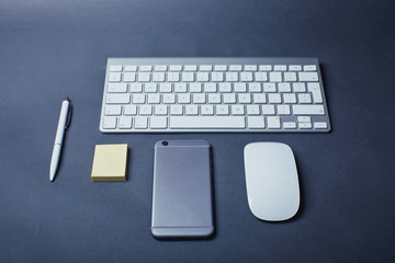 Office table with electronic gadgets. Smartphone, keyboard, mouse, pen and stickers.