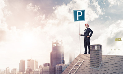 Young businessman with parking sign standing on brick roof. Mixe