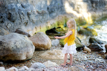 Cute little girl playing on a beach of lake Garda on warm and sunny summer day