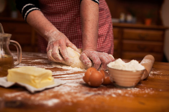Senior woman hands knead dough on table in home kitchen