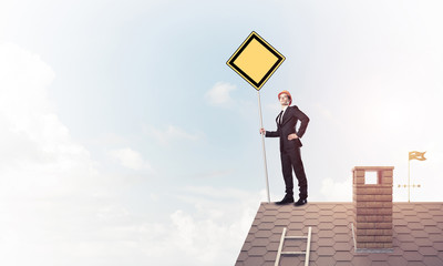 Young businessman on house brick roof holding yellow signboard. 