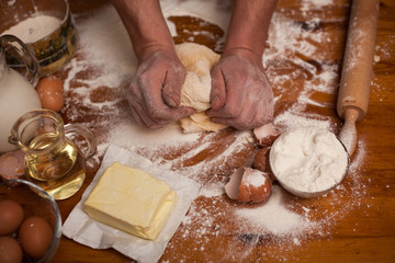 Senior man hands knead dough on table in home kitchen