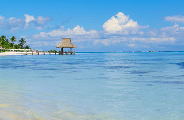 Tropical white sandy beach. Palm leaf roofed wooden pier with ga