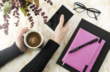 Female hands holding coffee and phone on work table