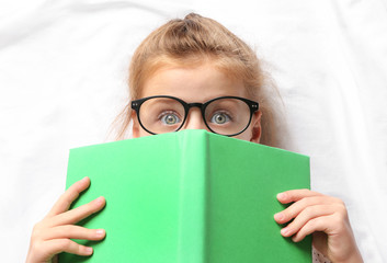 Cute girl with book lying on white sheets
