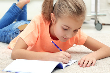Attractive little girl lying on the floor and writing in copybook
