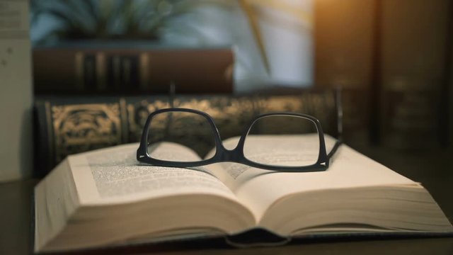 old books on desktop with modern glasses on open pages - vintage film style, smooth tracking shot