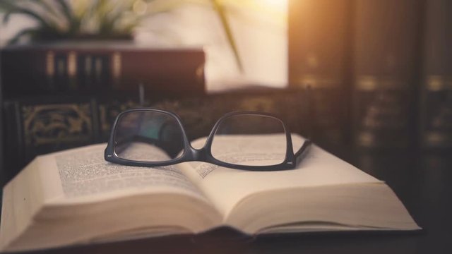 old books on desktop with modern glasses on open pages - vintage film style, smooth tracking shot