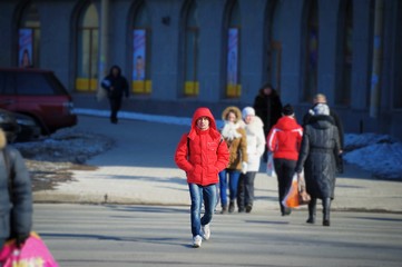 Daily life of urban residents in early spring. People go about their business on a bright Sunny day. Near the buildings in the shadow of snow. A man crossing the road