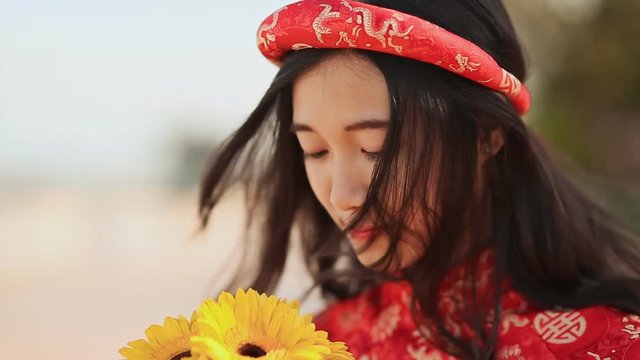Beautiful Vietnamese girl in red traditional dress Ao Dai with yellow flowers. Close-up.