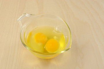 Two raw eggs in glass measuring cup on wooden table