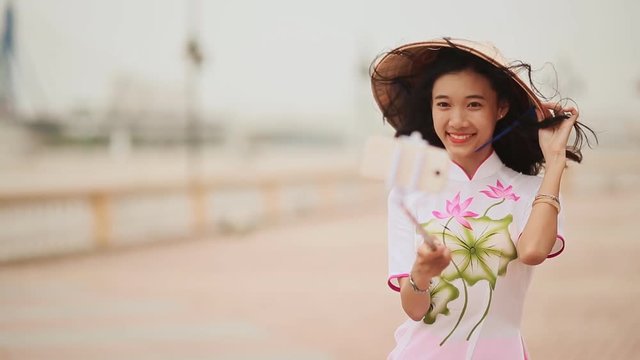 The girl in the Vietnamese national traditional costume photographs herself using the phone.