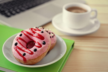 Delicious donuts with cup of coffee  and laptop on wooden table  closeup