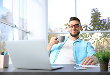 Fototapeta na wymiar Handsome young man drinking coffee while working with laptop at home