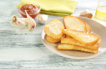 Plate with tasty garlic French bread slices on wooden table