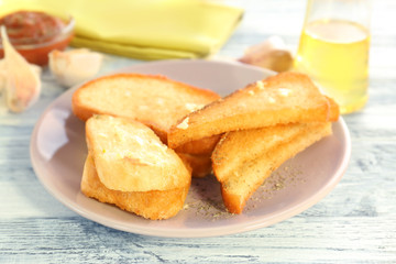 Plate with tasty garlic French bread slices on wooden table