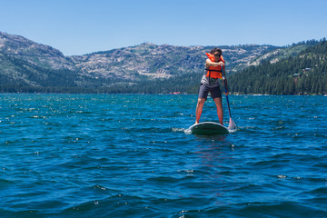 Young mixed race woman in hat and sunglasses paddle boards on a mountain lake in California