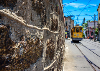 The stone wall, blue sky and old-fashioned yellow tram bonde going by tram tracks in Santa Teresa district of Rio de Janeiro, Brazil © shumoff
