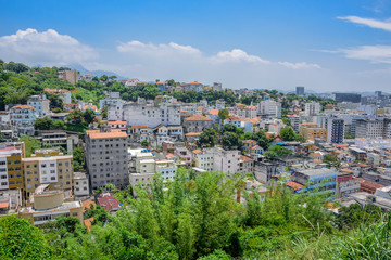 View of typical residential houses in the green area of Santa Teresa, blue sky and white clouds at hot, sunny day in Rio de Janeiro, Brazil