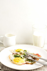 fried eggs on a white plate, glass of milk and a milk jug