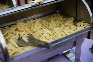 Pasta noodles sit in a silver chafing dish under a sliding cover at a party