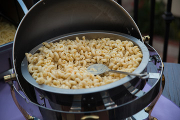 Pasta noodles sit in a silver chafing dish under a sliding cover at a party