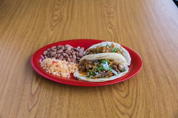 Fototapeta na wymiar Shredded pork tacos with side of rice and pinto beans on red plate on wooden table