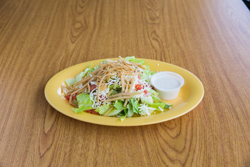 Caesar salad with cheese and side of dressing on white plate on wooden table