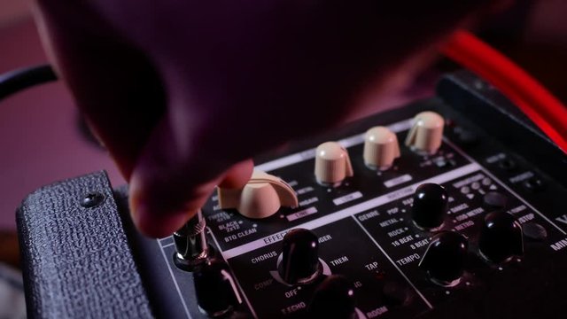 Man's hand inserts cable jack in guitar amp