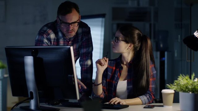 Late Night at the Office. Male and Female Colleagues Discuss Work Done on Her Personal Computer. In the Background Man Working at His Desk. Shot on RED Cinema Camera 4K (UHD). 