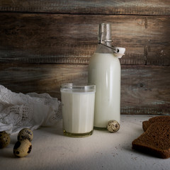 rustic still life with a bottle of milk, eggs and bread on background of rough wooden wall
