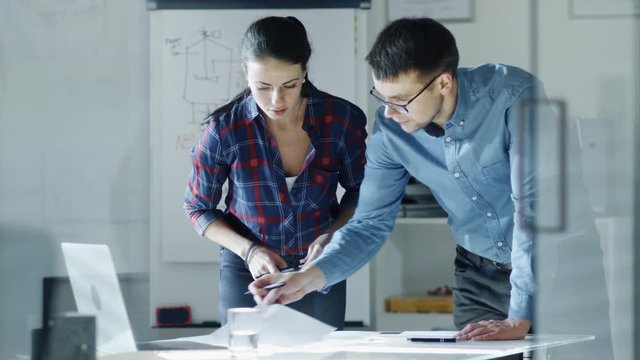 Male and Female Design Engineers Work on Drafts, Make Corrections and Discuss Their Project. On the Background Stands Whiteboard with Sketches. Shot on RED Cinema Camera 4K (UHD). 