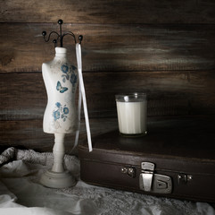 Still Life with an old suitcase, a glass of milk and a mannequin sewing on a background of a rough wooden wall