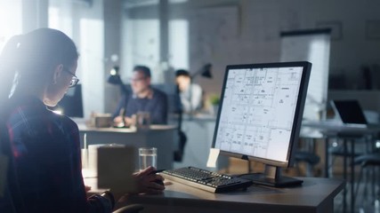 Late at Night in the Engineering Bureau Female Designer Works on a Personal Computer that Shows Blueprints of Her Project. In the Background Her Colleagues Working. Shot on RED Cinema Camera 4K (UHD). - Powered by Adobe