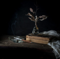 Still life with old books, dry leaves, and smoking a cigarette. dark background. vintage