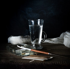 Still life with a water glass, ashtray and smoking a cigarette. dark background. vintage