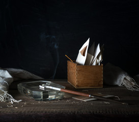 Still Life with a box of letters, and smoking a cigarette. dark background. vintage