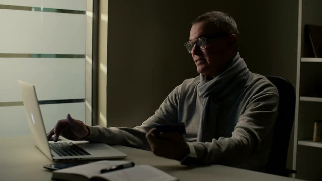 Middle aged man with grey hair use online shopping service and makes his first purchase with credit card in modern office