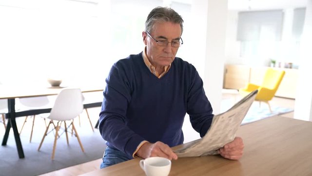 Smiling senior man with eyeglasses reading newspaper