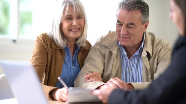 Senior couple meeting financial adviser and signing contract