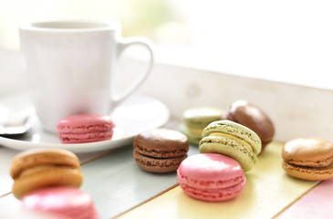 Delicious colorful macarons with cream and coffee cup. Coffee break scene with macaron candy and selective focus.