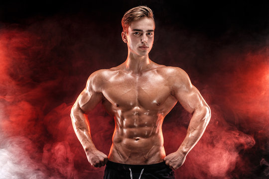 Strong Man Bodybuilder with Six Pack and perfect abs, shoulders, biceps, triceps and chest, personal fitness trainer flexing his muscles in red smoke.
