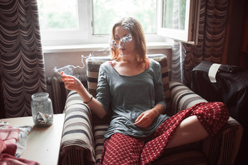 Young woman smoking indoors at a window (portrait with copy space)